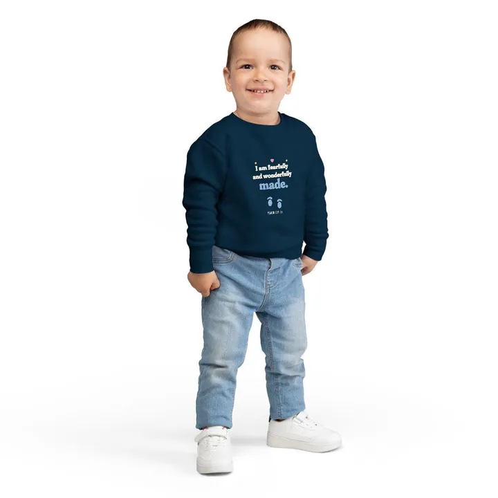 Smiling toddler wearing a navy crewneck sweatshirt with the I am fearfully and wonderfully made design with a pair of baby footprints, Psalm 139:14
