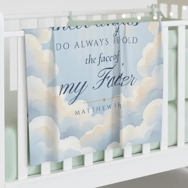 Blue baby swaddle blanket draped over a white crib rail, printed with the words do always behold the face of my Father, Matthew 18:10, in navy lettering over a pale blue watercolor sky of clouds and light